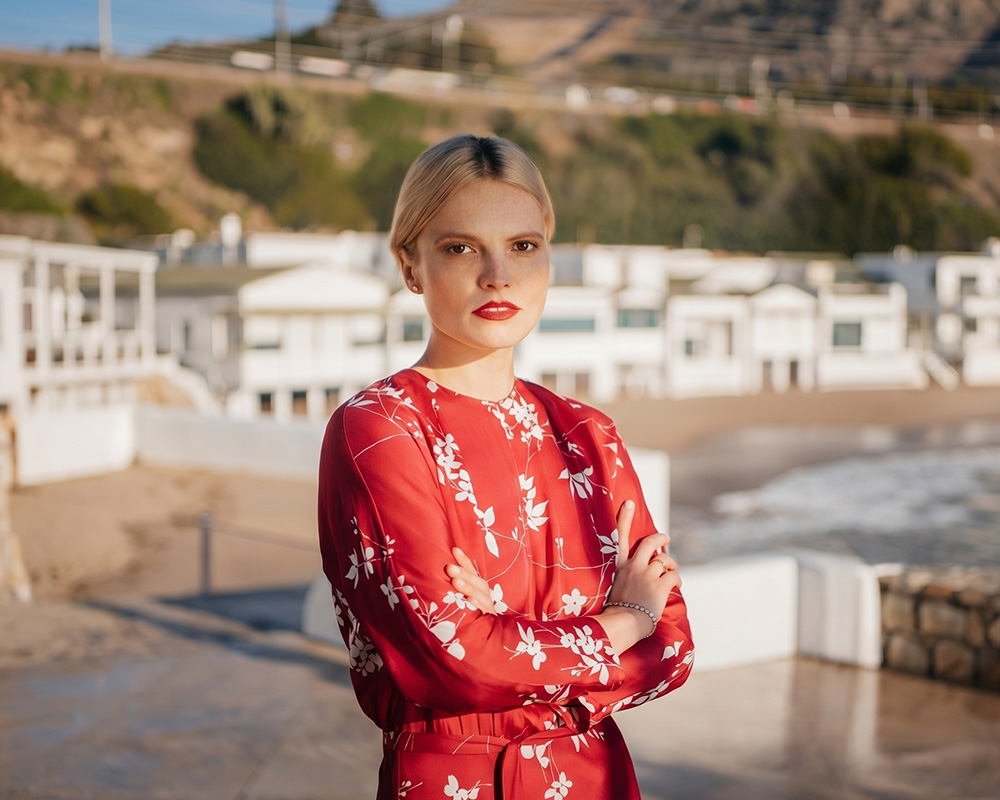 Kobieta ubrana w różową sukienkę w kwiaty marki Vistula stoi na tle plaży