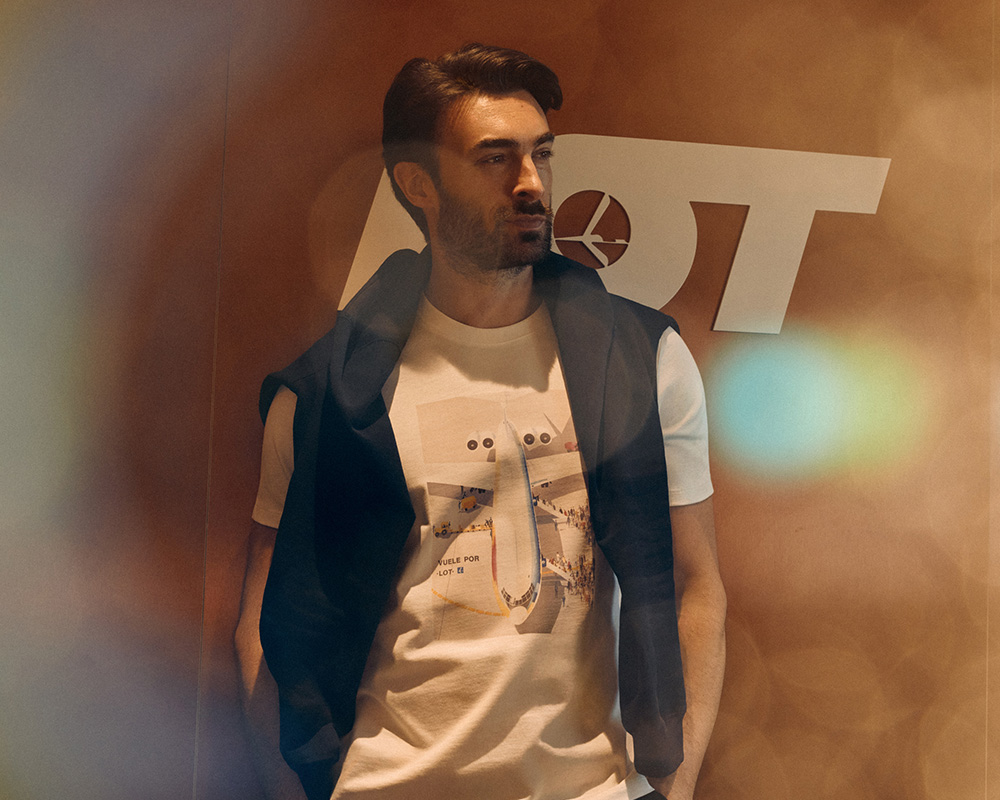 Mężczyzna w białym t-shircie i bluzie na tle logo LOT.
