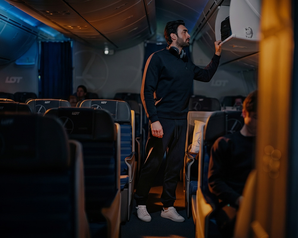 Mężczyzna w dresie wkładający bagaż podręczny do schowka w samolocie.